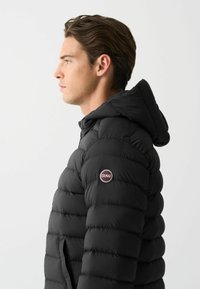 Melnā pūkainā jaka ar kapuci, ar quilted dizainu un Colmar logo uz piedurknes. Gluda tekstūra un pieguļoša forma.