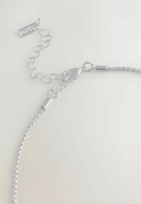 Zbliżenie na srebrny naszyjnik z łańcuszkiem z zapi�ęciem typu homar i regulowanym łańcuszkiem na jasnym tle.