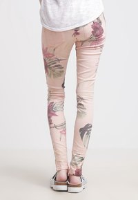 Leggings met bloemenpatroon in zachtroze, voorzien van tropische bladeren en bloemen. Materiaal lijkt rekbaar. Draagt metallic plateauzolen.
