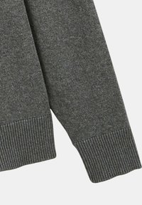 Manche de pull gris en maille avec un bord-côte. Le tissu présente une texture subtile avec un motif de tissage uniforme sur toute la surface.