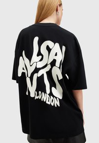 Černé oversize tričko vyrobené z bavlny, které má na zádech velký bílý potisk s nápisem "ALLSAINTS LONDON", kulatý výstřih.
