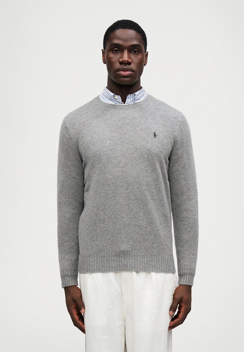 Suéter gris de lana con cuello redondo, puños y dobladillo acanalados, combinado con una camisa de cuadros azul y blanca con cuello debajo.