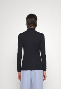 Schwarzes Langarm-Turtleneck-Oberteil aus glattem Stoff, figurbetontes Design, mit hohem Kragen und nahtlosen Schultern, kombiniert mit hellblauen Hosen.