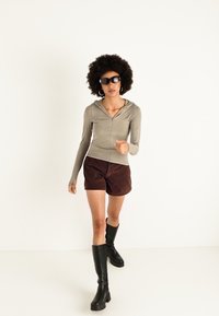 Langærmet, lysegrå zip-up trøje parret med brune shorts og knæhøje sorte støvler. Modellen bærer mørke solbriller og hoops øreringe.