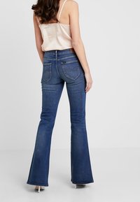 Uppvikta blå denimjeans med medelhög midja, som har bakfickor och en slät yta. Framhäver benens form.