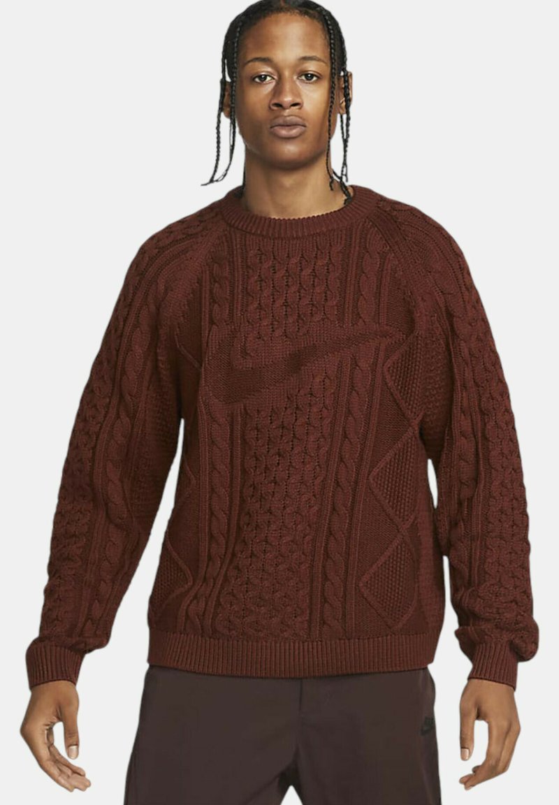 Bordeauxfaret striktrøje med teksturerede kabelmønstre, rund hals og ribkantede manchetter. Har et subtilt Nike-logo indarbejdet i strikdesignet.