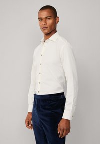 Witte lange mouwen shirt met een puntige kraag, bruine knopen en contrasterende manchetten, gecombineerd met donkerblauwe corduroybroek met een riemdetail.