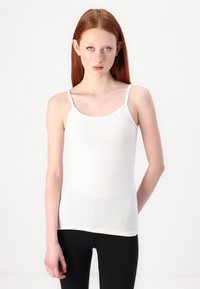 Hvit tettsittende cami med tynne stropper, laget av myk, elastisk stoff. Jevn tekstur og rund halsringning, kombinert med svarte leggings.