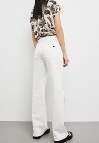 Jeans anchos blancos de tiro alto, con bolsillos traseros y una etiqueta negra. Combinados con una blusa de manga corta con estampado floral en beige y negro.