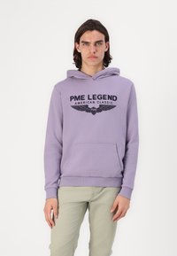 Fialová mikina s predným klokaním vreckom, s nápisom "PME LEGEND AMERICAN CLASSIC" a grafikou krídiel. Mäkká tkanina a rebrované manžety.