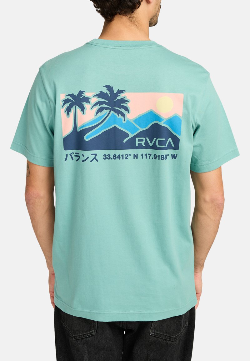 Mintgroene t-shirt met een graphic van palmbomen, bergen en een zon op de achterkant, met tekst en coördinaten in donker marineblauw.