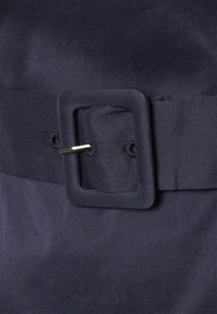 Granatowy pas materiałowy z prostokątną klamrą i srebrnym ząbkiem. Gładka tekstura z wzmocnionymi szwami wzdłuż krawędzi.