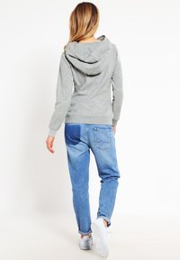 Sweat-shirt à capuche gris et jean denim bleu clair, avec une jambe fuselée et une poche appliquée. Look décontracté complété par des baskets blanches.