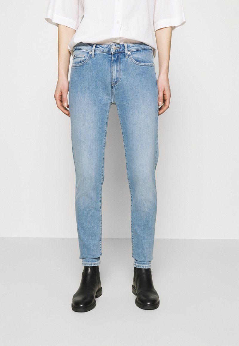 Jean bleu clair en denim, avec une coupe slim, un design à cinq poches et une braguette zippée. Accompagné de bottines noires.