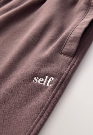 Kokvilnas sporta bikses klusinātā purpursarkanā krāsā ar mīkstu tekstūru, kreisajā priekšpusē ar mazu baltu izšūtu logotipu "self.".