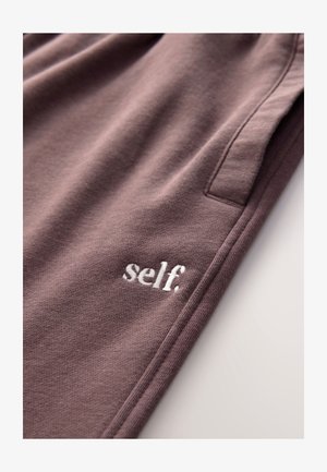 Kokvilnas sporta bikses klusinātā purpursarkanā krāsā ar mīkstu tekstūru, kreisajā priekšpusē ar mazu baltu izšūtu logotipu "self.".