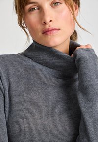 Pulover gri cu guler înalt, cu mâneci lungi și guler pliat. Materialul pare moale, cu o textură medie și o croială lejeră.