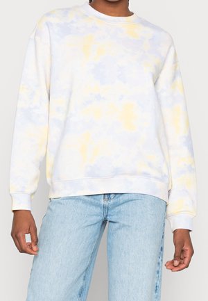 Personne portant un sweat-shirt à manches longues tie-dye jaune clair et bleu, avec un jean bleu clair.