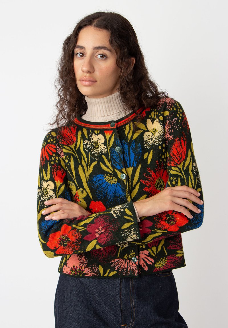 Cardigan court à motif floral de couleur vert foncé, orné de fleurs rouges, bleues et jaunes. Fermeture à boutons à l'avant avec un col en rib de contraste.
