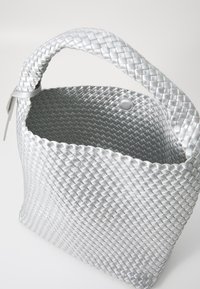 Ασημένια πλεκτή τσάντα με στρογγυλή λαβή, ανοιχτό πάνω, λεία υφή, και στρογγυλή βάση, με λεπτομέρεια κουμπιού με πρέζα.