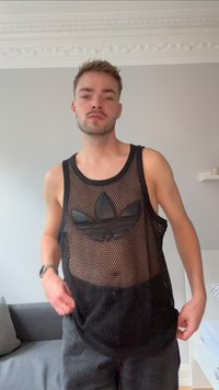 Tricou din plasă negru, cu decolteu circular, având un logo Adidas texturat de culoare neagră. Purtați-l peste pantaloni închisi, pe un fundal gri.