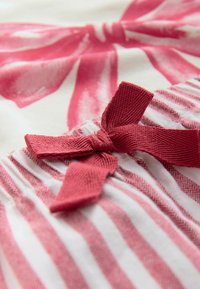 Textil med rosa rosettkant på en vit bakgrund, med djärva, målade rosa motiv och växlande tunna och tjocka ränder.