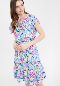 Blumenkleid mit hellblauem Hintergrund und Mustern in Pink, Lila und Grün, kurzen Ärmeln, einem Bindekragen und einem gestuften Saum.