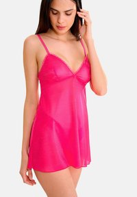 Camisole en maille rose avec une texture transparente, des bretelles réglables et une bordure en dentelle à volants au niveau du cou, tombant jusqu'à mi-cuisse.