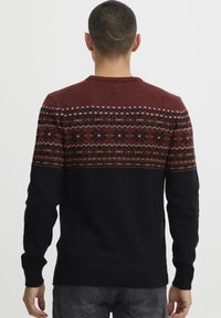 Strikkegenser med en maroon og mønstrete yoke, som går over til en ensfarget svart kropp. Har lange ermer og ribbede mansjetter og hem.