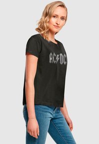 Schwarzes Baumwoll-T-Shirt mit kurzen Ärmeln, das ein silbernes AC/DC-Logo in fetter, metallischer Schrift auf der Brust zeigt. Klassische Passform und Rundhalsausschnitt.