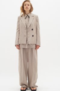 Beige randig kostym med dubbelknäppt kavaj och vida byxor, tillverkad av ett lätt tyg med en slät textur.