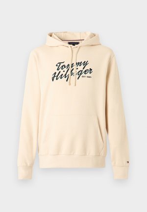 Beige Tommy Hilfiger Kapuzenpullover mit Fronttasche, Kordelzugkapuze und Logotext "Tommy Hilfiger EST. 1985" auf der Brust.