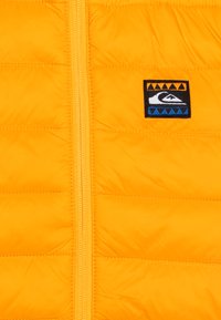 Giacca a vento gialla con zipper frontale e un patch con logo ricamato, caratterizzato da accenti geometrici nei colori blu, arancione e nero.