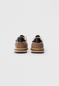 Pair of brown and beige sneakers with black heel accents, viewed from the back on a white background.
