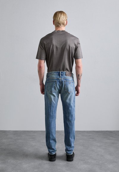 Gray patterned t-shirt, relaxed fit, paired with light blue straight-leg jeans. Notable feature: logo on the back of the waistband.