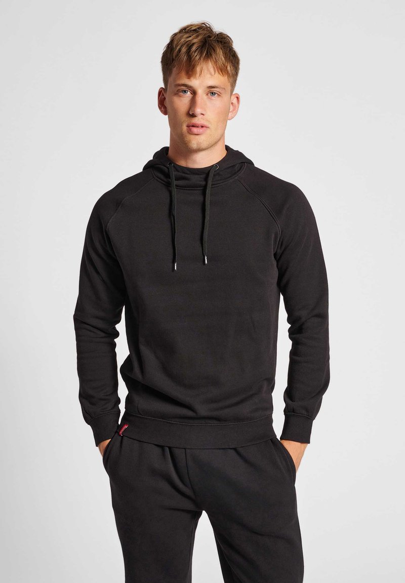Svart hoodies i mjukt material, med dragsko i huvan, ribbade muddar och en känguruficka. Enkelt, minimalistiskt design.