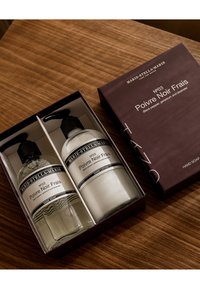 Set di due flaconi con pompa: sapone per le mani trasparente e lozione per le mani bianca. Etichette con testo nero su entrambi. Imballati in una scatola viola scura.