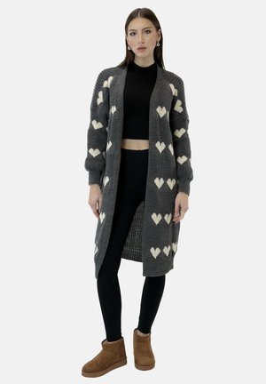 Cardigan grigio lavorato a maglia con motivi a cuore bianchi, aperto sul davanti, tessuto testurizzato, maniche lunghe, abbinato a un crop top nero e leggings.