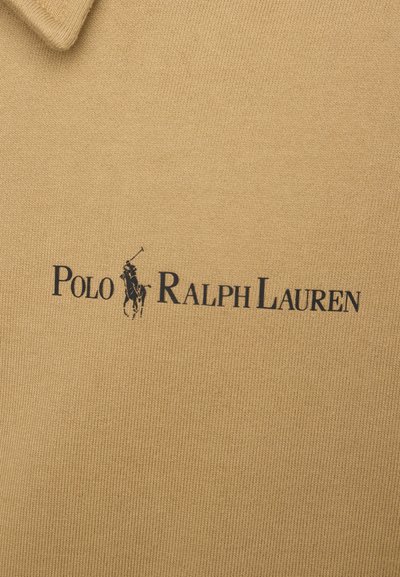 Beige polo shirt with a knitted texture, featuring a black logo reading "POLO RALPH LAUREN" and an image of a polo player above the text.