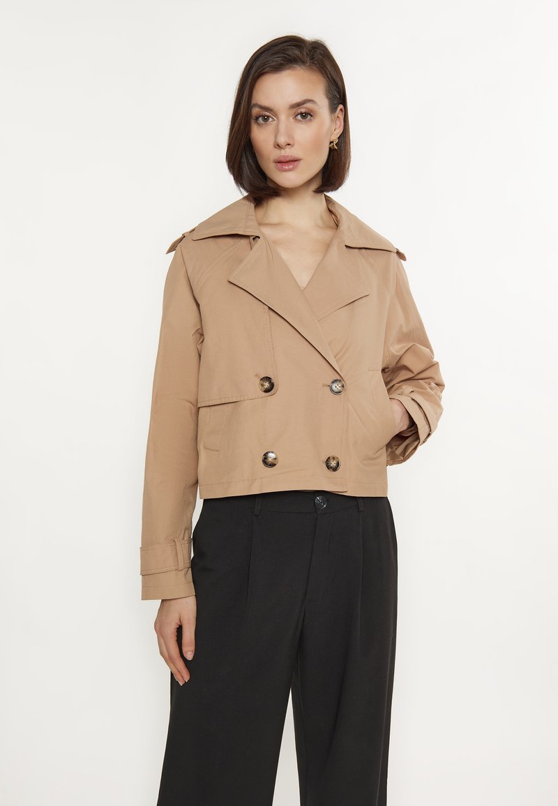 Beige cropped Jacke mit doppelter Knopfleiste, großen Revers und dekorativen Knöpfen. Glatte Textur, geeignet für verschiedene Outfits.