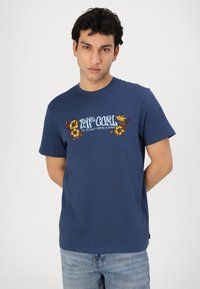 Granatowa bawełniana koszulka z krótkim rękawem, z florystycznym wzorem oraz napisem "Rip Curl" w jasnoniebieskim kolorze. Klasyczny krój z okrągłym dekoltem, casualowy fason.