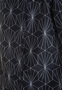 Tessuto nero con un motivo geometrico bianco di esagoni interconnessi e linee radiali, che mostra un dettaglio di cucitura.