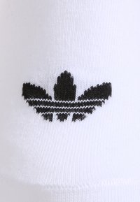 Biezu zeķu ar melnu izšūtā Adidas trefoil logotipu, kas sastāv no trim lapām un trim horizontālajām svītrām zem tā.