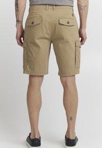 Shorts cargo beiges en mélange de coton, avec plusieurs poches, une coupe décontractée et des ourlets, portés avec des chaussures noires.