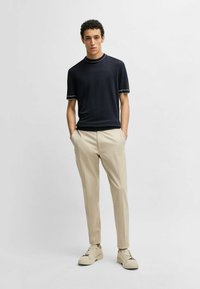 Navy crew-neck knitted t-shirt with white trim, paired with beige tailored pants and light-colored sneakers. Smooth fabric, modern fit.