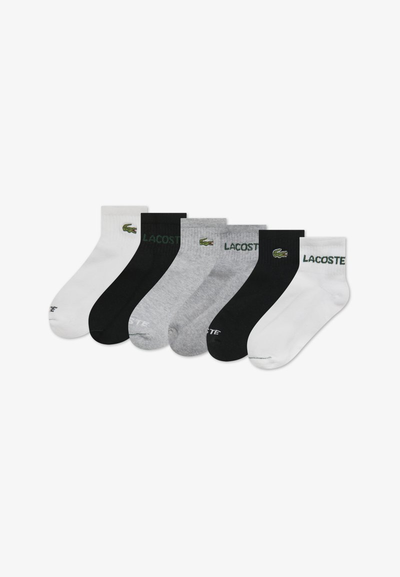 Six paires de chaussettes en blanc, noir et gris, avec un logo Lacoste vert. Chaque paire est dotée d'un bord-côte et d'une texture lisse.