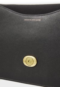 Sac en cuir noir présentant une texture lisse, une fermeture ronde en doré et des détails en relief "CUIR PLEINEFLEUR AUTHENTIQUE".