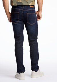 Jeans de mezclilla azul oscuro con corte ajustado, con costuras naranjas, dos bolsillos traseros y una etiqueta de cuero en la cintura. Combinados con zapatillas blancas.