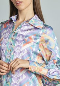 Blusa di seta con vivaci motivi geometrici in colori pastello, con colletto a punta, chiusura a bottoni e maniche arricciate.