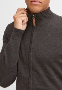 Dunkelgrauer Zip-Hoodie mit ribbeligem hohen Kragen und Bündchen, ausgestattet mit einem Leder-Zipper und glattem Strickmuster.